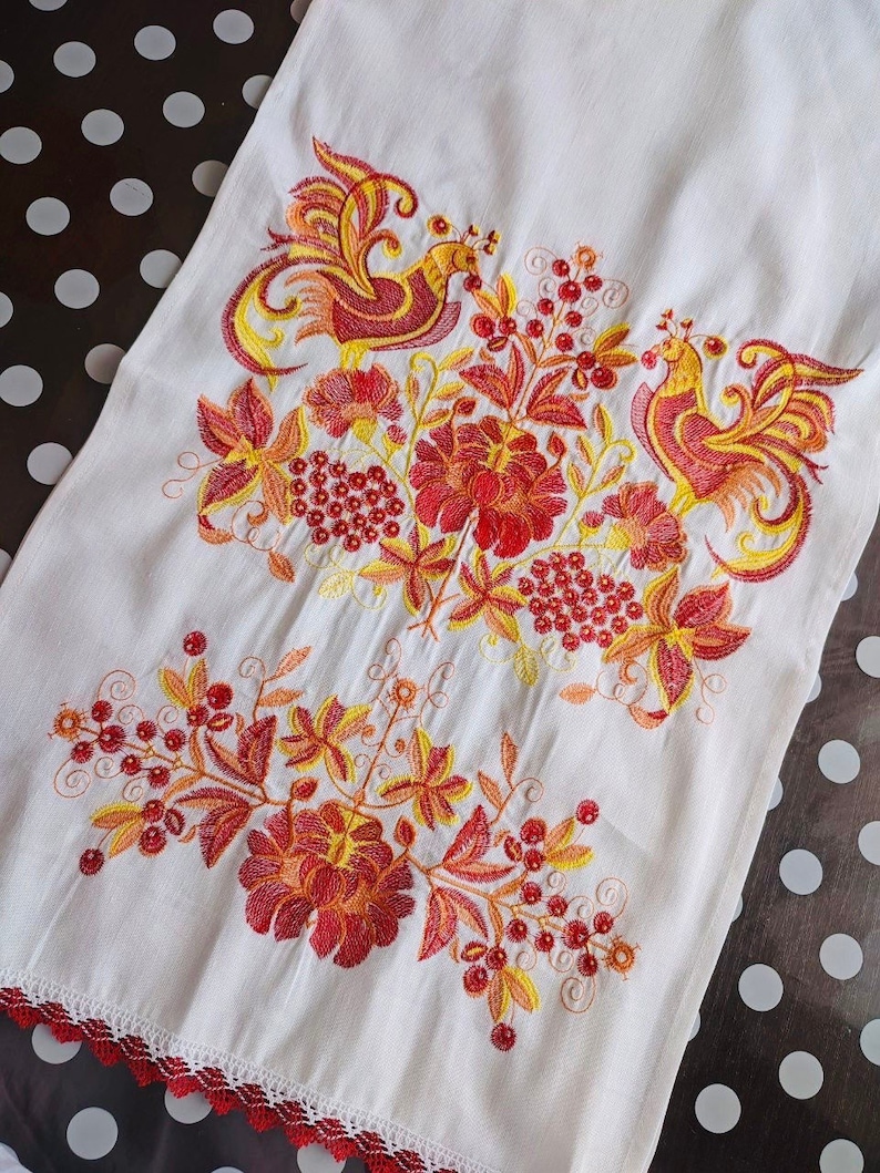 Peut inclure: Serviette en lin blanc avec broderie vibrante repr&eacute;sentant deux oiseaux stylis&eacute;s, des fleurs et des baies dans des tons de rouge, orange et jaune. Le bord inf&eacute;rieur est orn&eacute; d'une bordure en dentelle rouge. Textile d&eacute;coratif.