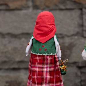 Puede incluir: Una mu&ntilde;eca hecha a mano con un pa&ntilde;uelo rojo, un chaleco verde, una camisa blanca y una falda de cuadros rojos y blancos. La mu&ntilde;eca lleva una peque&ntilde;a cesta verde.