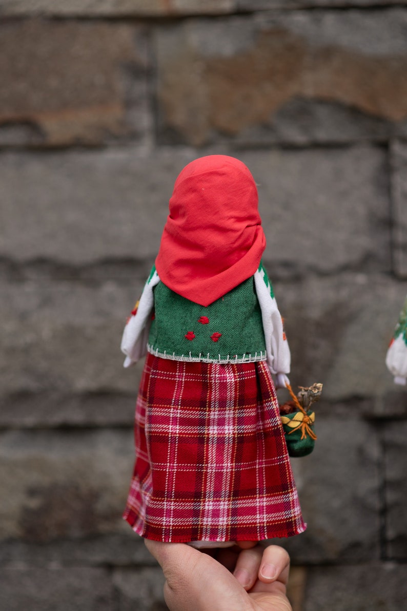 Puede incluir: Una mu&ntilde;eca hecha a mano con un pa&ntilde;uelo rojo, un chaleco verde, una camisa blanca y una falda de cuadros rojos y blancos. La mu&ntilde;eca lleva una peque&ntilde;a cesta verde.