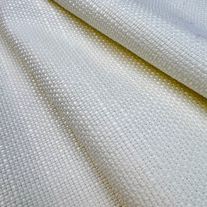 May include: Close-up of a textured, off-white fabric with a woven pattern. The fabric has a subtle sheen and a slightly irregular texture, creating a sense of depth and visual interest. The weave is tight, suggesting durability.