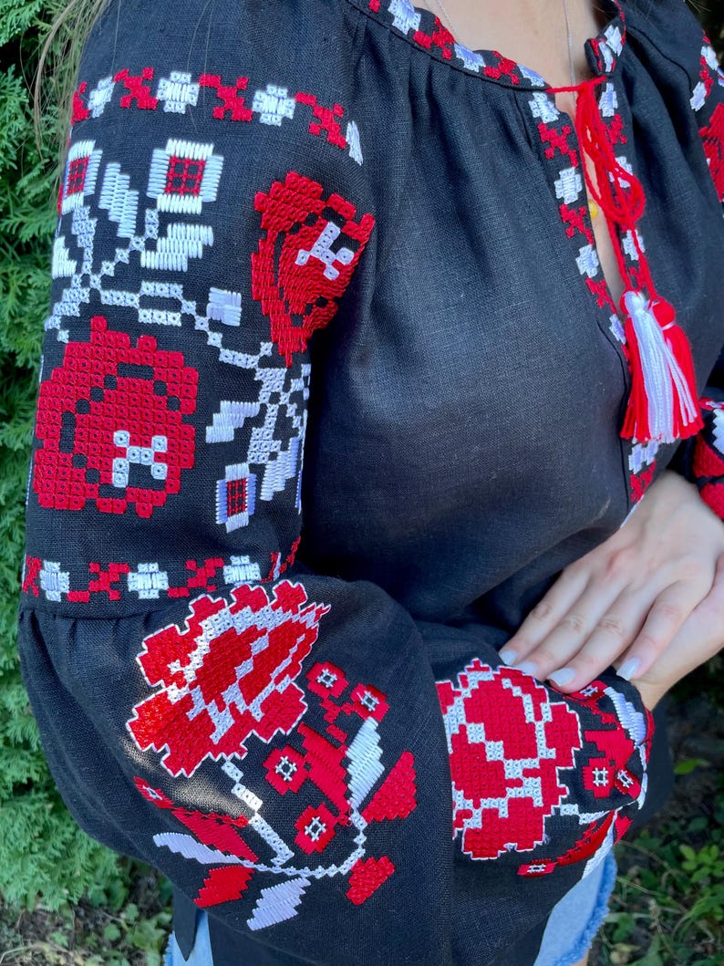 Puede incluir: Blusa de lino negra con patrones florales bordados en rojo y blanco. El bordado es de estilo ucraniano tradicional.