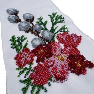 May include: A white fabric panel featuring a beaded floral design. The design incorporates red, pink, and green beads, creating flowers and leaves. The beads are arranged in a pattern that resembles embroidery.