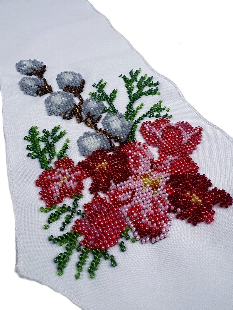 May include: A white fabric panel featuring a beaded floral design. The design incorporates red, pink, and green beads, creating flowers and leaves. The beads are arranged in a pattern that resembles embroidery.