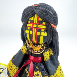 K&ouml;nnte beinhalten: Handgemachte Puppe mit schwarzen Garnhaaren und einem gelb-rot gemusterten Gesicht. Die Puppe tr&auml;gt ein schwarzes Kleid mit gelbem Spitzensaum und einem roten Band. Eine Perlenkette ziert den Hals der Puppe.