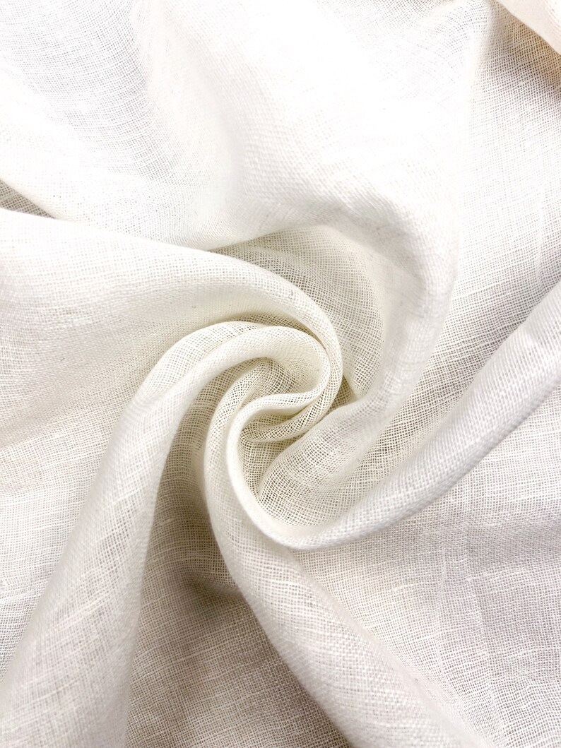 Puede incluir: Tela de lino blanco con una superficie suave y texturizada. La tela est&aacute; doblada y drapeada, creando un aspecto suave y fluido.