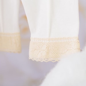 May include: White garment with a delicate lace trim. The lace is a light cream color and has a delicate floral pattern.