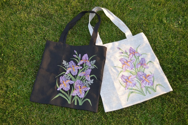 May include: Two tote bags with embroidered purple iris flowers. One bag is black and the other is white.