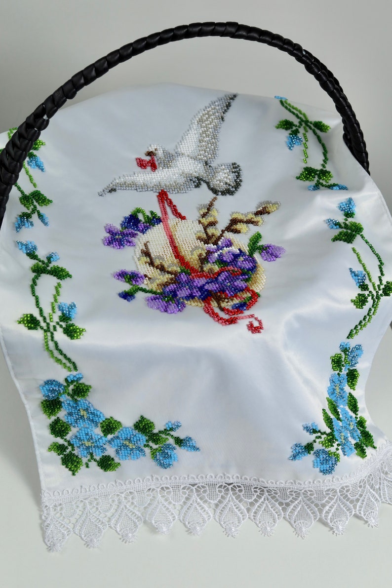 May include: White satin basket liner featuring a beaded design of a dove, flowers, and an egg. The liner has a white lace trim.