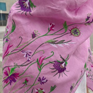 Puede incluir: Una bufanda de lino rosa con dise&ntilde;os florales bordados en tonos de morado, verde y blanco.