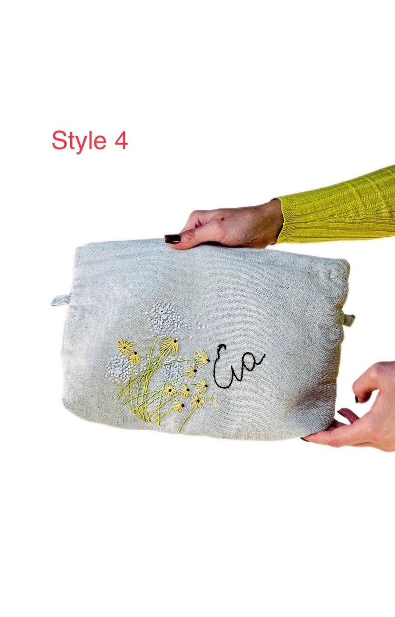 May include: A light gray canvas pouch with a floral embroidery design and the name "Eva" embroidered in black thread.