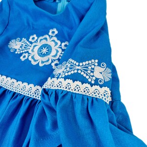 K&ouml;nnte beinhalten: Ein blaues Kleid mit wei&szlig;en gestickten Blumenmustern und wei&szlig;en Spitzenbesatz an den &Auml;rmeln.