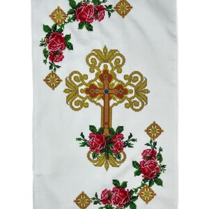 May include: White fabric with a gold cross embroidered in the center. The cross is surrounded by a wreath of red roses. The fabric has a white background with a gold border.