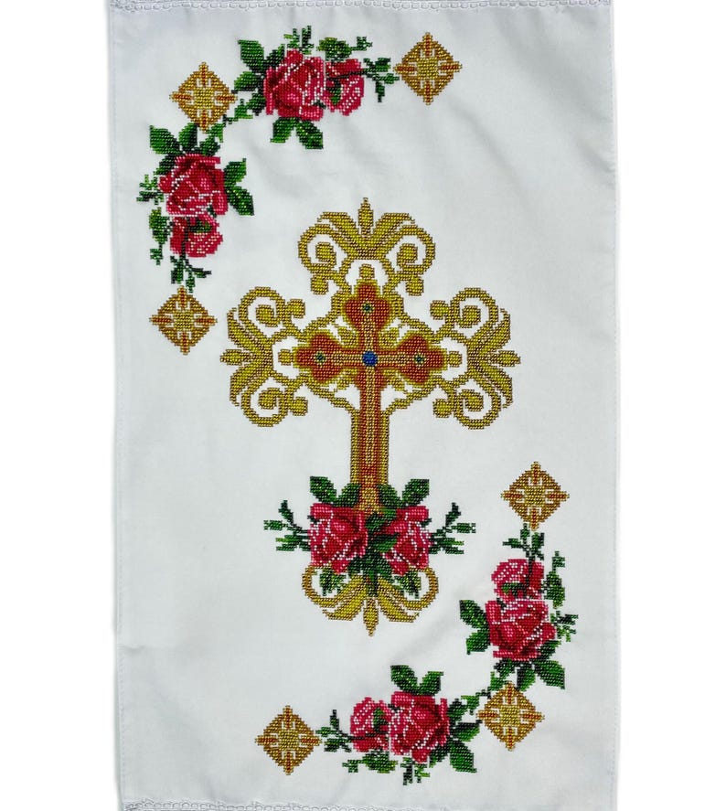 May include: White fabric with a gold cross embroidered in the center. The cross is surrounded by a wreath of red roses. The fabric has a white background with a gold border.