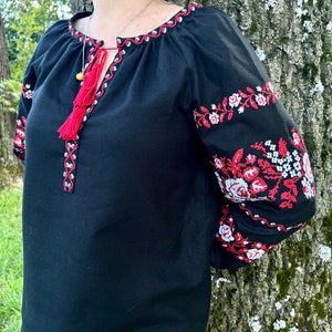 K&ouml;nnte beinhalten: Schwarze bestickte Bluse mit roten und wei&szlig;en Blumendesigns. Die Bluse hat ein Quasten-Detail am Ausschnitt.