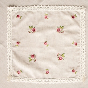 May include: A white linen tea towel with a delicate lace border and embroidered pink roses.