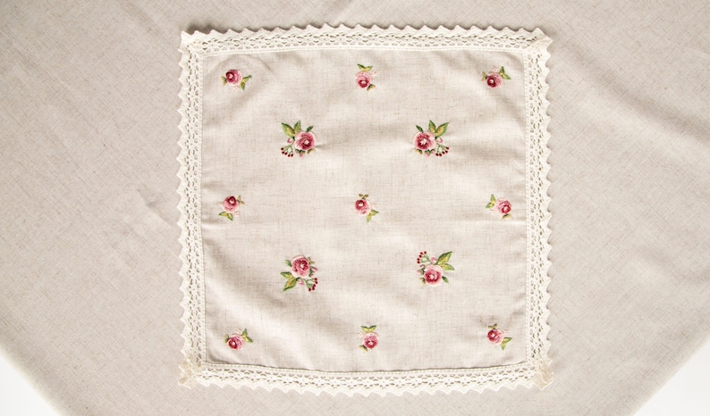 May include: A white linen tea towel with a delicate lace border and embroidered pink roses.