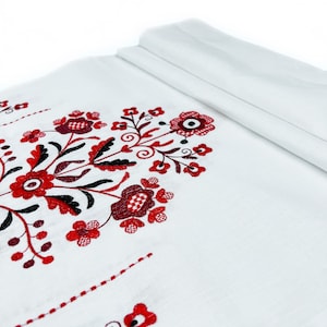 K&ouml;nnte beinhalten: Wei&szlig;er Stoff mit roten und schwarzen gestickten Blumenmustern. Die Stickerei zeigt stilisierte Blumen und Bl&auml;tter.