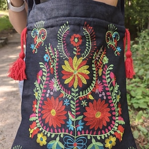 May include: Black tote bag with colorful embroidered floral design. The flowers are red, yellow, blue, green, and pink. The bag has red tassels on the sides.