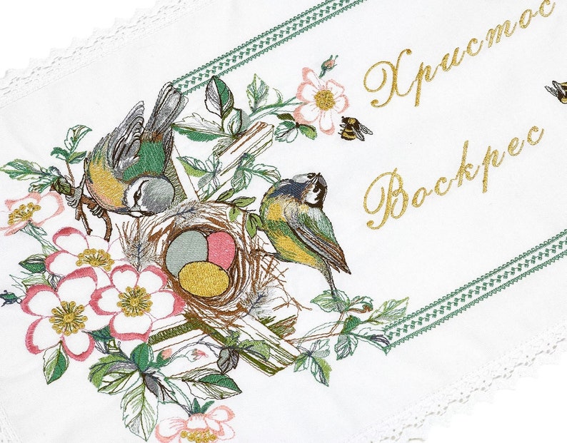 以下が含まれることがあります： 花と鳥のデザインが施された白い刺繍生地。刺繍には、2羽の青と黄色の鳥、卵のある巣、ピンクの花、そして金色の文字で「Христос Воскрес」という文字が描かれています。緑色の縁とレースが縁を飾っています。