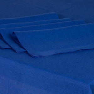 May include: Four folded, cobalt blue linen napkins arranged on a matching tablecloth. The napkins are neatly stacked, showcasing their crisp edges and textured surface. The deep blue color creates a cohesive and elegant table setting.