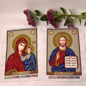 May include: Two embroidered religious icons on white fabric. One depicts Mary and Jesus, the other Jesus holding a book. The icons feature gold, red, blue, and brown beadwork. Text in Russian is visible at the top and bottom of each icon.