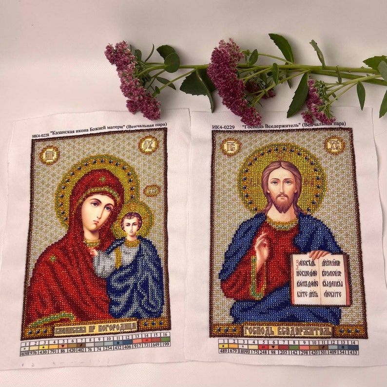 May include: Two embroidered religious icons on white fabric. One depicts Mary and Jesus, the other Jesus holding a book. The icons feature gold, red, blue, and brown beadwork. Text in Russian is visible at the top and bottom of each icon.