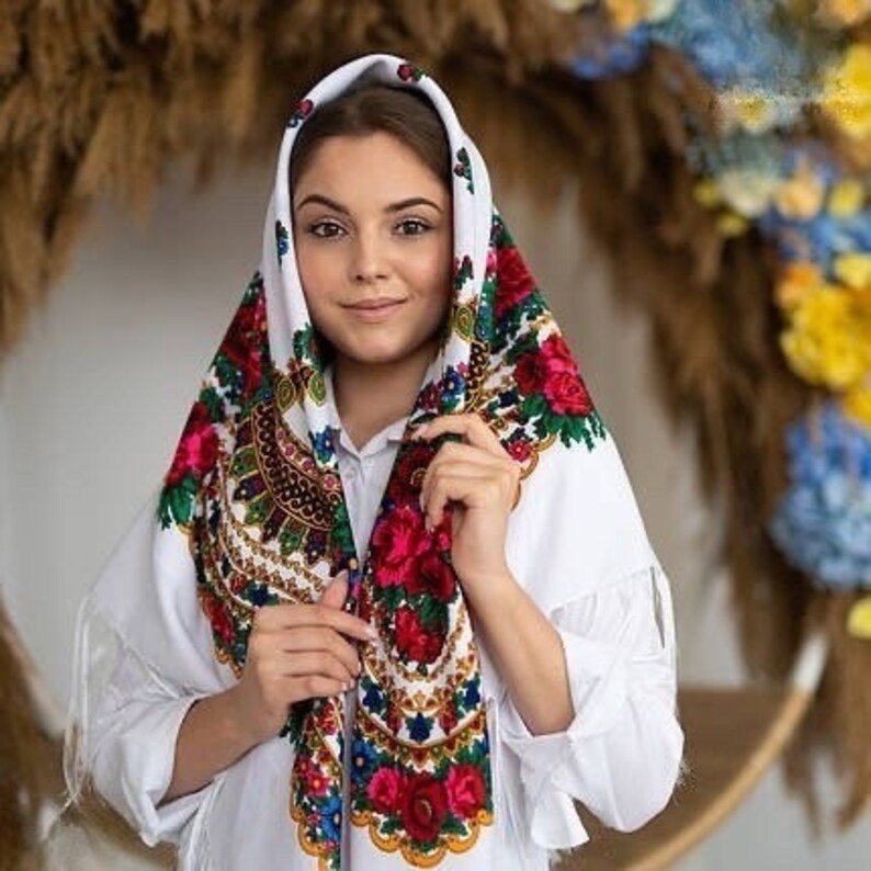 May include: A white headscarf with a colorful floral pattern. The scarf is folded and tied around the head, with the floral pattern visible on the front and sides.