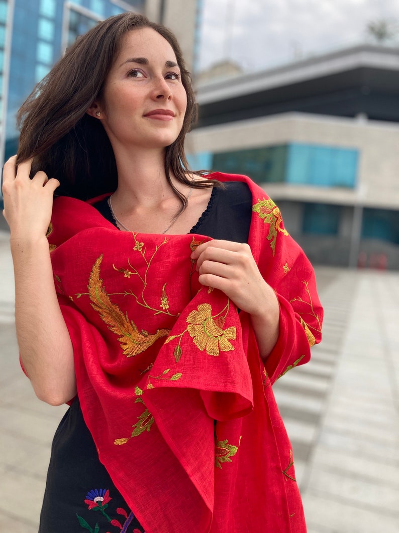 Puede incluir: Una mujer lleva una chal roja con bordados dorados. El chal tiene un dise&ntilde;o floral con p&aacute;jaros y hojas. La mujer lleva un vestido negro con estampado floral.
