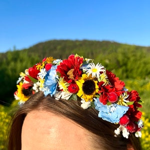 Pode incluir: Uma faixa de cabe&ccedil;a floral com flores vermelhas, amarelas, azuis e brancas. A faixa de cabe&ccedil;a &eacute; feita de flores artificiais e est&aacute; sendo usada por uma pessoa.