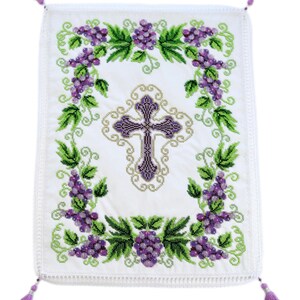 Puede incluir: Pa&ntilde;o rectangular blanco bordado con un dise&ntilde;o central de cruz morada. La cruz est&aacute; rodeada por un borde dorado y enmarcada por hojas verdes y racimos de uvas moradas. Cuatro borlas moradas est&aacute;n unidas a las esquinas.