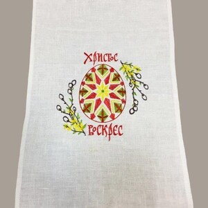 Peut inclure: Serviette de cuisine en lin blanc avec une bordure brod&eacute;e rouge. La serviette pr&eacute;sente un &oelig;uf de P&acirc;ques brod&eacute; rouge, jaune et vert avec le texte "Христос Воскрес" en rouge.