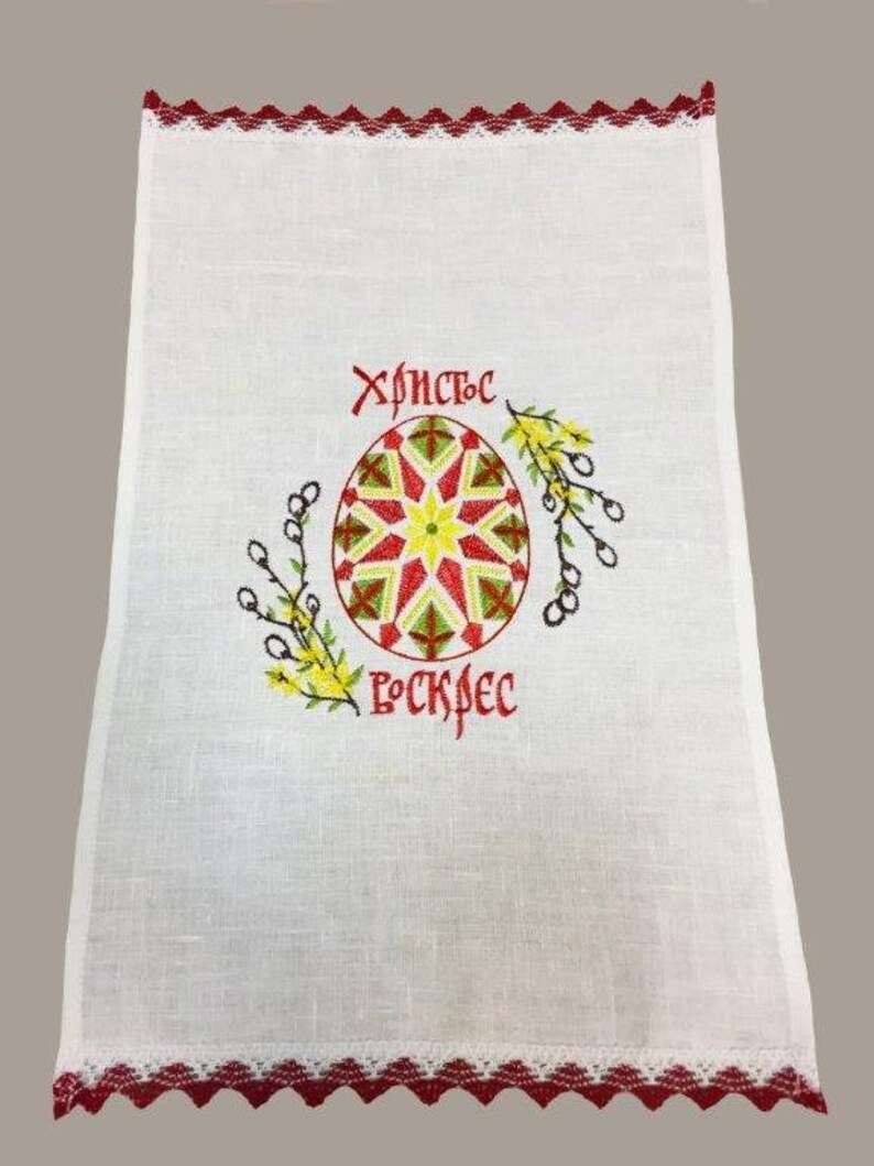 Peut inclure: Serviette de cuisine en lin blanc avec une bordure brod&eacute;e rouge. La serviette pr&eacute;sente un &oelig;uf de P&acirc;ques brod&eacute; rouge, jaune et vert avec le texte "Христос Воскрес" en rouge.