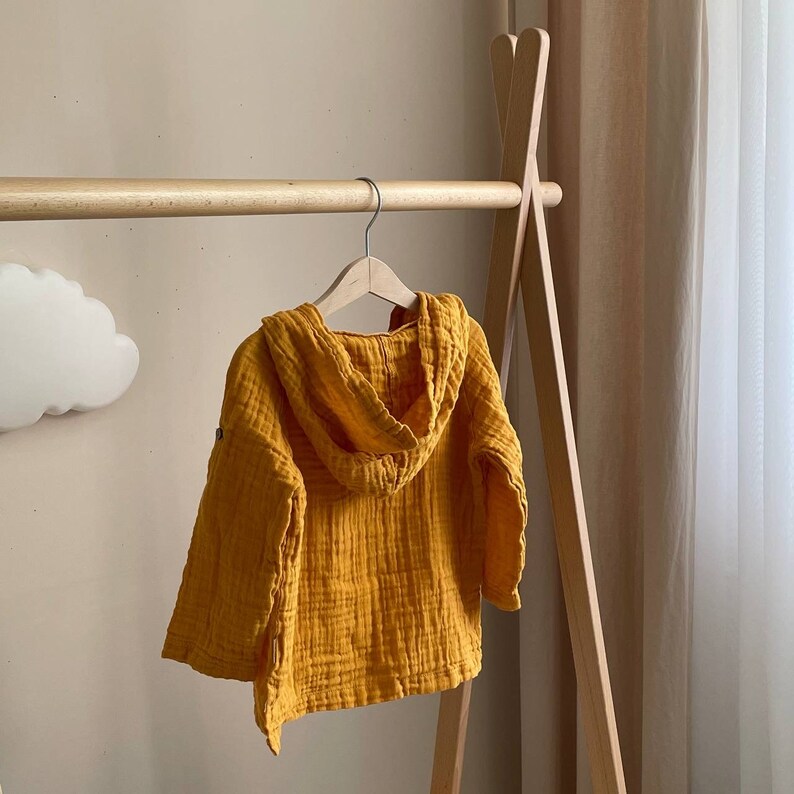 May include: A yellow hooded sweatshirt with a waffle texture. The sweatshirt is hanging on a wooden hanger.
