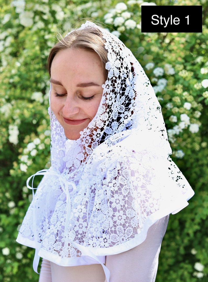 May include: White lace head covering with a floral pattern. The lace is gathered at the neck and tied with a ribbon. Style 1.