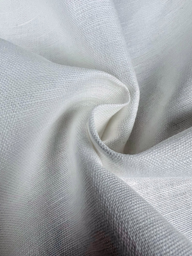 May include: White linen fabric with a textured weave. The fabric is folded and draped, showing its soft and smooth texture.