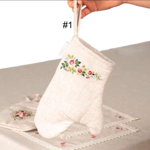 May include: Off-white oven mitt with a floral embroidery design in pink, red, and blue. The mitt has a loop for hanging and is part of a kitchen set. The text "#1" is visible.