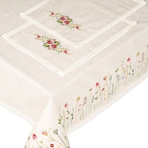 May include: A white linen tablecloth with delicate floral embroidery. The tablecloth features a lace trim and a smaller embroidered square in the center. The embroidery is in shades of pink, green, and blue.