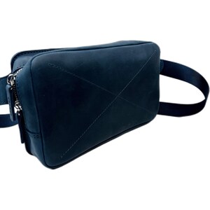 May include: A dark blue leather fanny pack with a zipper closure and a strap. The bag has a stitched X design on the front.