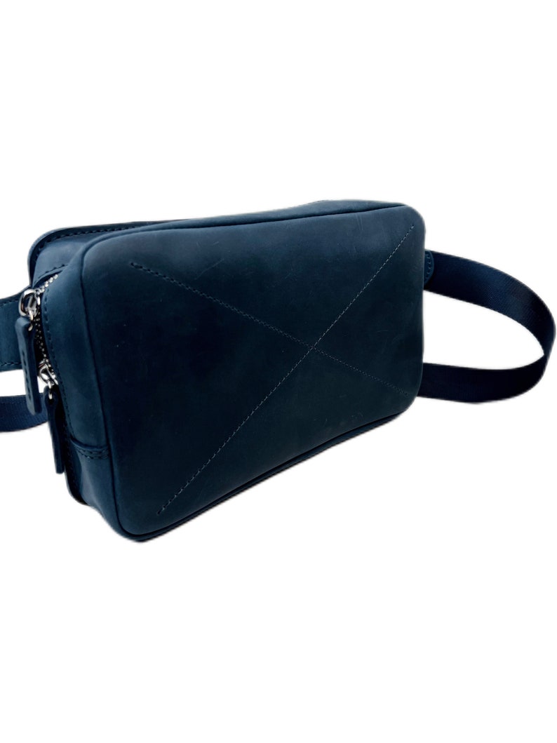 May include: A dark blue leather fanny pack with a zipper closure and a strap. The bag has a stitched X design on the front.