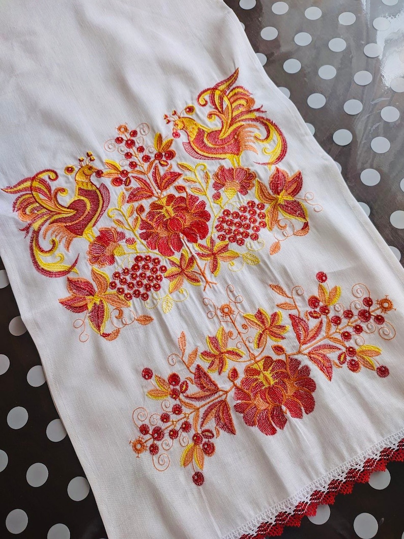 May include: White linen tea towel with red and yellow embroidered floral design featuring two stylized birds. The embroidery includes a floral pattern with berries and leaves.