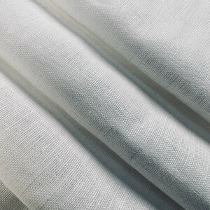 K&ouml;nnte beinhalten: Nahaufnahme eines hellgrauen Stoffes mit sichtbarer Textur und Falten. Der Stoff scheint Leinen oder ein &auml;hnliches gewebtes Material zu sein. Die Falten erzeugen Schatten und Lichtreflexe und verleihen dem Bild Tiefe. Der Stoff wird wahrscheinlich f&uuml;r Heimdekoration oder Kleidung verwendet.