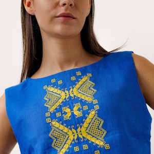 May include: A sleeveless blue linen top with a yellow embroidered geometric pattern.