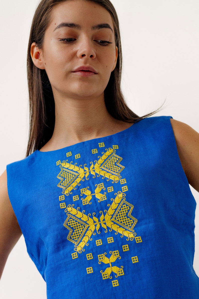May include: A sleeveless blue linen top with a yellow embroidered geometric pattern.