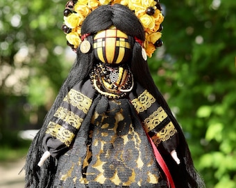 May include: A black and yellow folk doll with long black hair, wearing a black and gold dress with lace trim and a yellow flower crown. The doll has a painted face with black eyes and a yellow and black striped pattern.