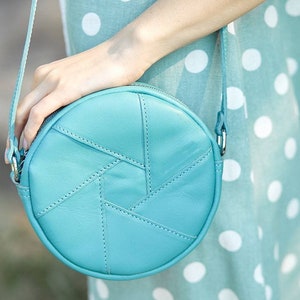 Puede incluir: Un bolso de hombro redondo de cuero azul claro con un patr&oacute;n geom&eacute;trico. El bolso tiene una cremallera y una correa de cadena plateada.