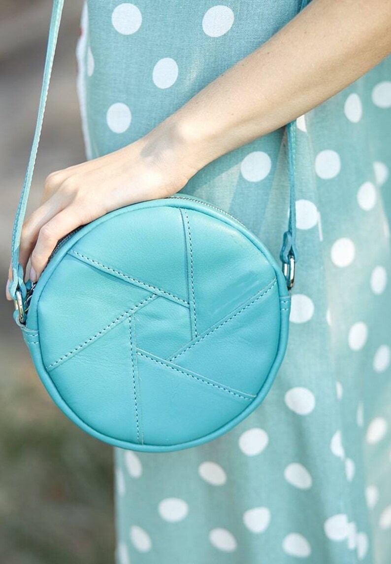 Puede incluir: Un bolso de hombro redondo de cuero azul claro con un patr&oacute;n geom&eacute;trico. El bolso tiene una cremallera y una correa de cadena plateada.