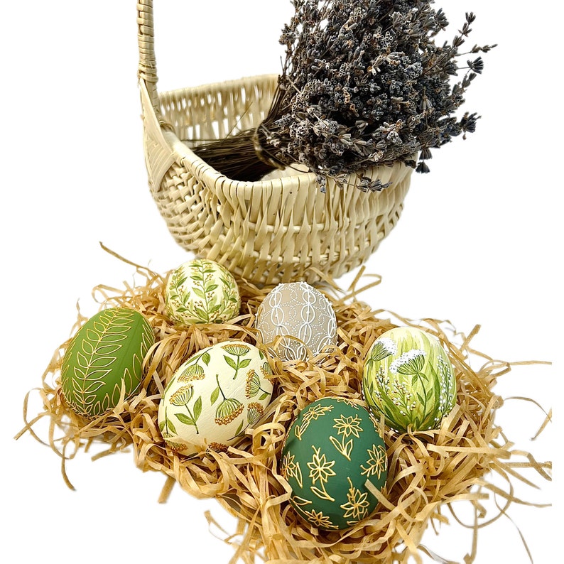 May include: Six hand-painted Easter eggs in a wicker basket with lavender. The eggs are decorated with green, white and gold floral patterns.