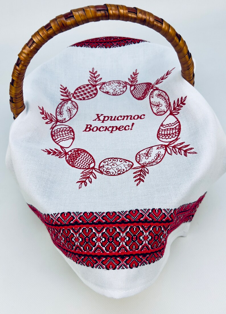 May include: White fabric Easter basket with a red embroidered wreath of eggs and the text "Христос Воскрес!" (Christ is Risen!). The basket has a brown wicker handle.