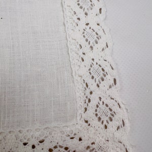 Pu&ograve; includere: Primo piano di un quadrato di lino bianco con un delicato bordo in pizzo traforato. Il pizzo presenta un motivo geometrico ripetuto, che aggiunge un tocco di eleganza al tessuto semplice e strutturato. L'estetica generale &egrave; pulita e classica.