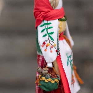 Puede incluir: Una mu&ntilde;eca tradicional folcl&oacute;rica con un pa&ntilde;uelo rojo, una blusa blanca bordada y una falda de cuadros rojos y negros. La mu&ntilde;eca lleva una cesta verde con flores secas.